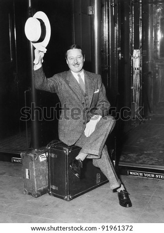 Portrait of a businessman sitting on his suitcases on a platform in front of a train