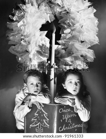 Two children sitting under a wreath holding a Christmas story book