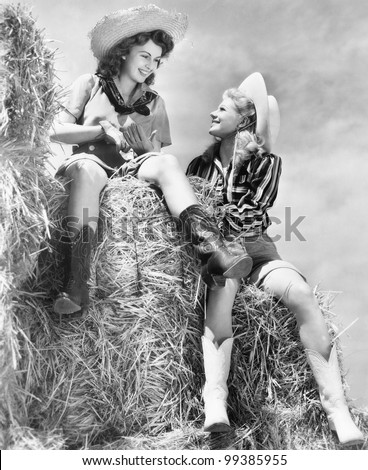 Two women in cowboy hats sitting on a haystack
