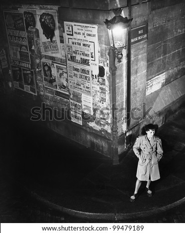 High angle view of a young woman waiting next to a lantern on a dark street corner