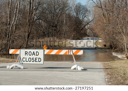 Road closed sign with flooded road and the Maumee river in the background.