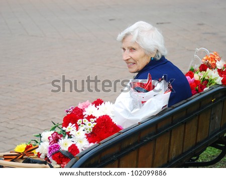 MOSCOW, RUSSIA - MAY 09: Senior woman war veteran smiling, sitting on a bench holding flowers. Victory Day celebration on Poklonnaya Hill (Moscow) on May 09, 2012 in Moscow, Russia.