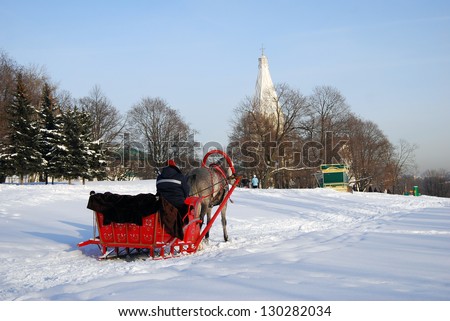 MOSCOW, RUSSIA - JANUARY 27: Red sleigh pulled by a horse in a winter park. Traditional Russian winter fun. Ascension cathedral seen at background. Taken on 27.01.2013 in Kolomenskoye, Moscow, Russia.
