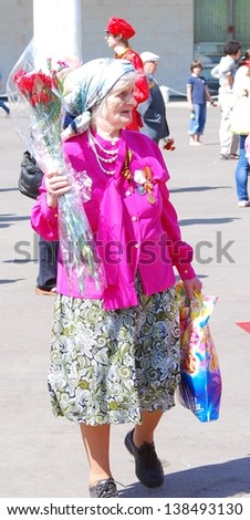 MOSCOW, RUSSIA - MAY 09: Old veteran woman walks with red carnation flowers. Victory Day celebration on May 09, 2013 in Moscow.