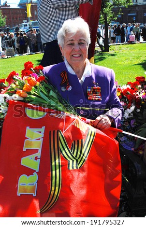 MOSCOW - MAY 09, 2014: Senior woman veteran outdoors portrait. She holds a red flag and looks at camera. Victory Day celebration in Moscow.