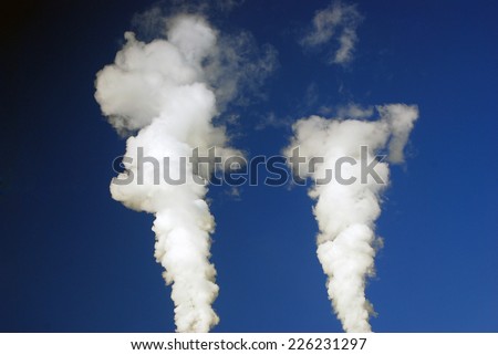 Industrial smoke coming out of fuming tubes. Blue sky background.