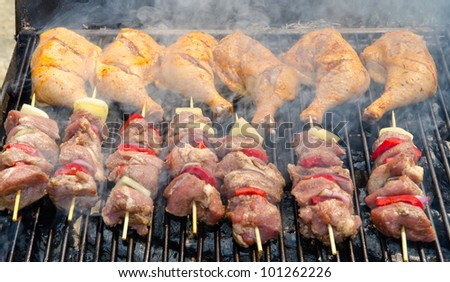 Skewers and chicken legs cooking on a grill on a sunny day.