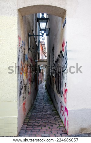 Narrow street in Freiburg with graffiti drawings on walls and old lanterns.