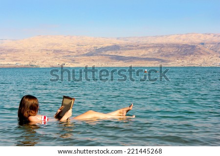 young woman reads a book floating in the waters of the Dead Sea in Israel