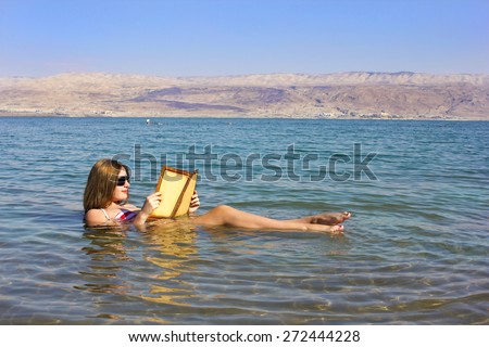 beautiful young woman reads a book floating in the waters of the Dead Sea in Israel