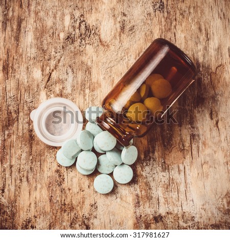 Blue-green pills spilled from open cans of dark glass lying on an old table.