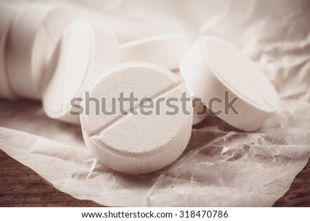 White pills in a paper wrapper lying open on a wooden table.