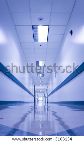 Long, empty corridor in a hospital or office building, with the ceiling lights reflected on the shiny floor. Image naturally almost monochromatic, bluish tint suggesting a cold, sterile environment