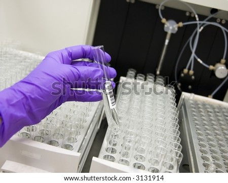 Gloved hand picking up a test tube.  Focus on test tube label
