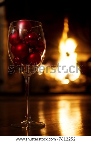 Glass of wine with red baubles in front of the fireplace.  Selective focus, golden glow from the fire.