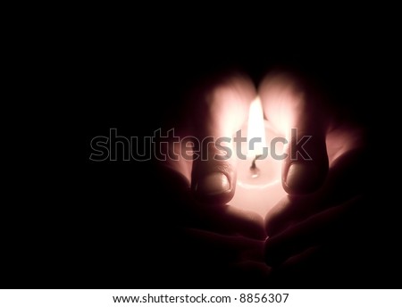 Hands holding a lit canle - low key image, warm colors