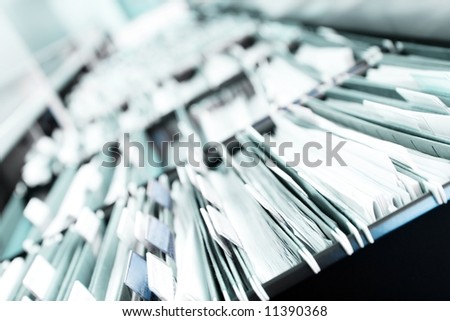 Multiple rows of filing cabinets in an office or medical establishment, overflowing with files.  Narrow depth of field to emphasize the \