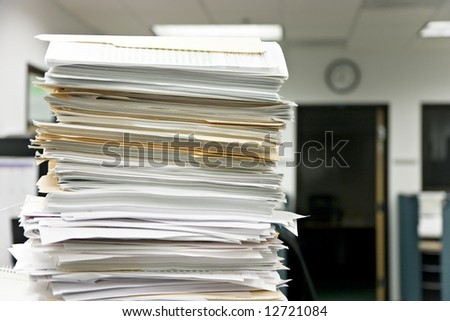 Close-up of a high pile of files, overwhelming the office in the background