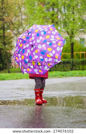 Back view of toddler girl with umbrella outdoors at rainy day