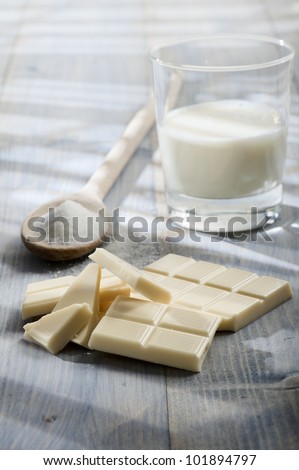 white chocolate bar with sugar and glass of milk, on wooden table lighted by the sun