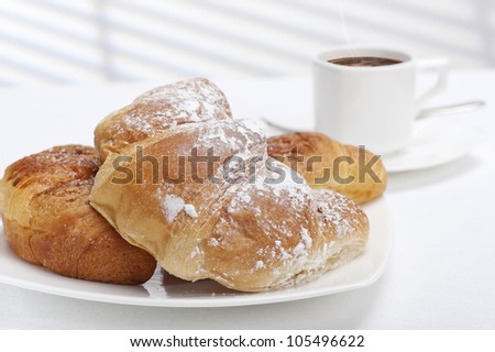fresh bakery croissants with cup of coffee, on white tablecloth and sunlight on backdrop