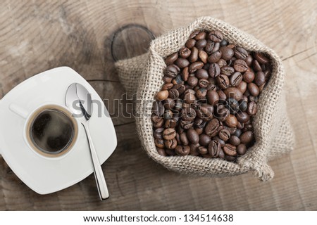 coffee beans in jute bag on wooden table with cup of coffee