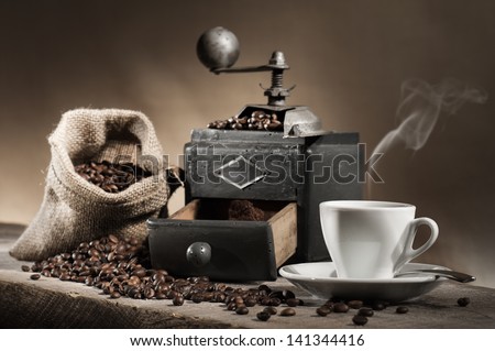 hot cup of coffee with coffee grinder and coffee beans in jute bag on wooden table