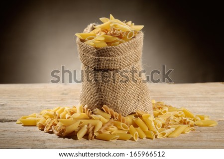 jute bag with variety of uncooked pasta on wooden table