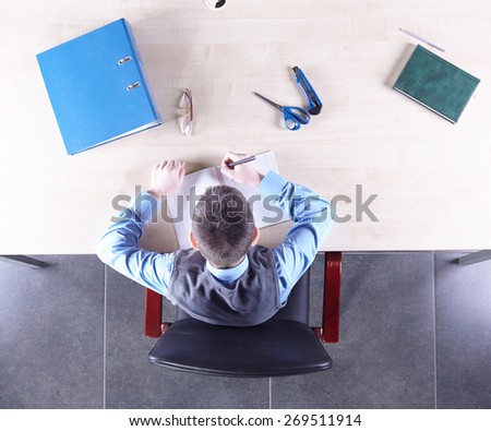 Boy sitting in a chair at the office table. Top view