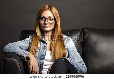 Attractive young woman in glasses sitting on black sofa on black background