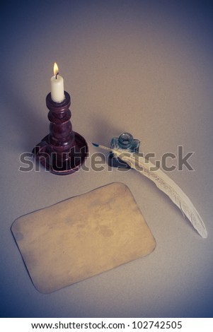 Candle in vintage candlestick, quill and inkwell, old paper blank