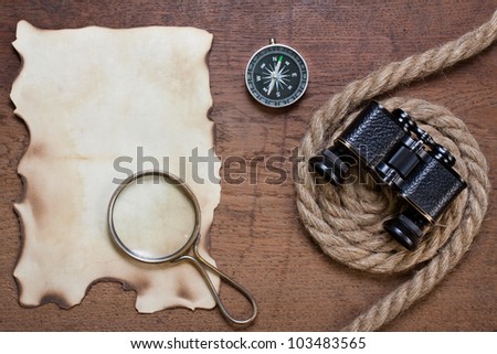 Burnt paper, compass, magnifying glass, binoculars, rope on the old wooden background