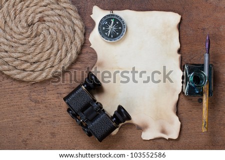 Burnt paper, compass, binoculars, ink and pen, rope on the old wooden background