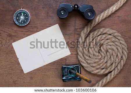 Old postcard, inkwell, compass, binoculars, rope on the old wooden table