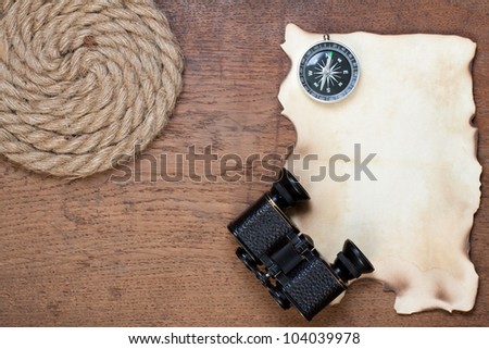 Compass, burnt grunge paper, binoculars and rope on wooden background
