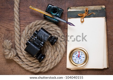 Antique notebook, compass, rope, inkwell and pen on the old wood background