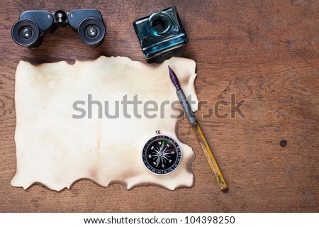 Burnt paper, compass, binoculars, ink and pen on the oak wood background