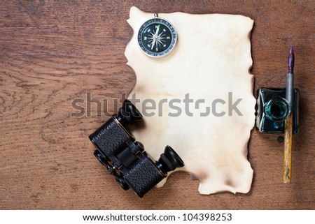 Burnt paper, compass, binoculars, ink and pen on the oak wood background