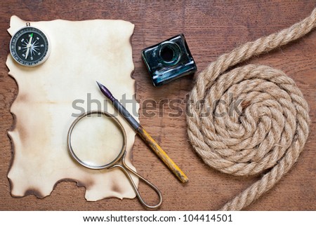 Magnifying glass, compass, burnt paper, inkwell and pen, rope on the old wood