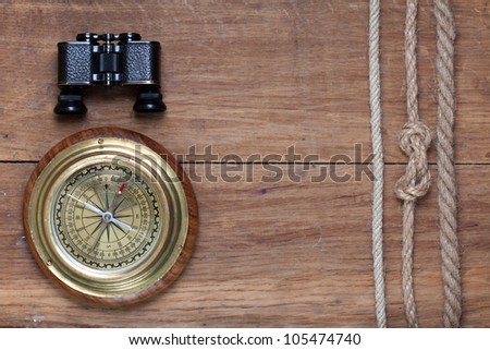 Bronze compass, binoculars and rope on wooden background