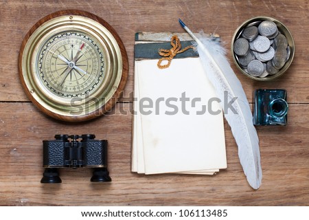 Compass, antique notebook, binoculars, quill and inkwell, coins on wood