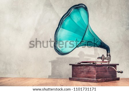 Vintage antique aged aquamarine gramophone phonograph turntable on wooden table front concrete wall background with its shadow. Retro old style filtered photo