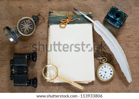 Old notebook, compass, binoculars, pocket watch, quill and inkwell, magnifying glass on wooden texture