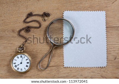 Vintage pocket watch, paper frame and magnifying glass on wood
