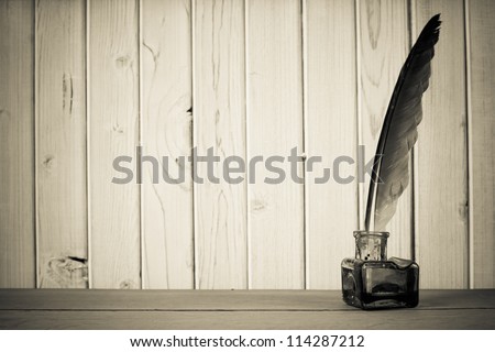 Vintage quill and inkwell on the table in front of wooden wall background