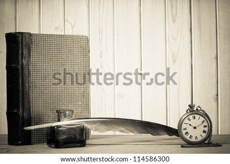 Quill pen and inkwell, book, antique pocket watch, on the table in front of wooden wall background