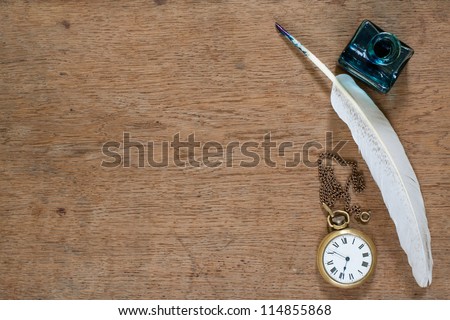 Quill pen and inkwell, old pocket watch on wooden texture background