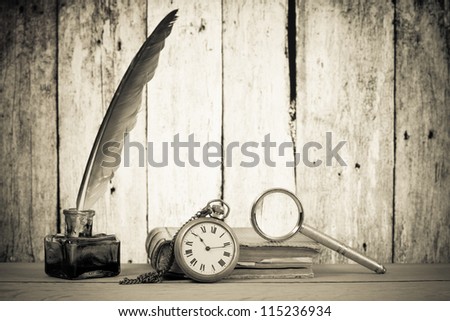 Pocket watch, quill pen and inkwell, book, magnifying glass on the table in front of grunge wooden background