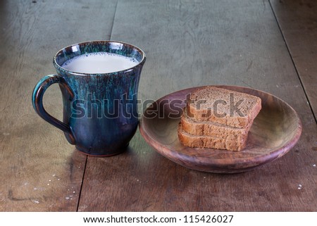 Cup of milk and bread in wooden plate on old oak table