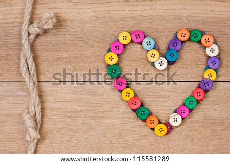 Heart shape of color buttons and rope knot connection on wooden background